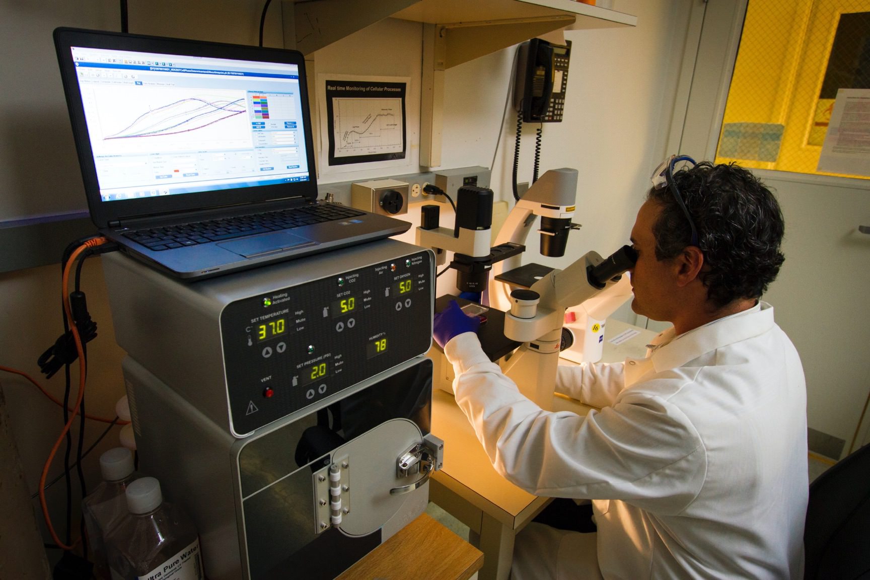 Scientist in labcoat sitting at desk looking through microscope
